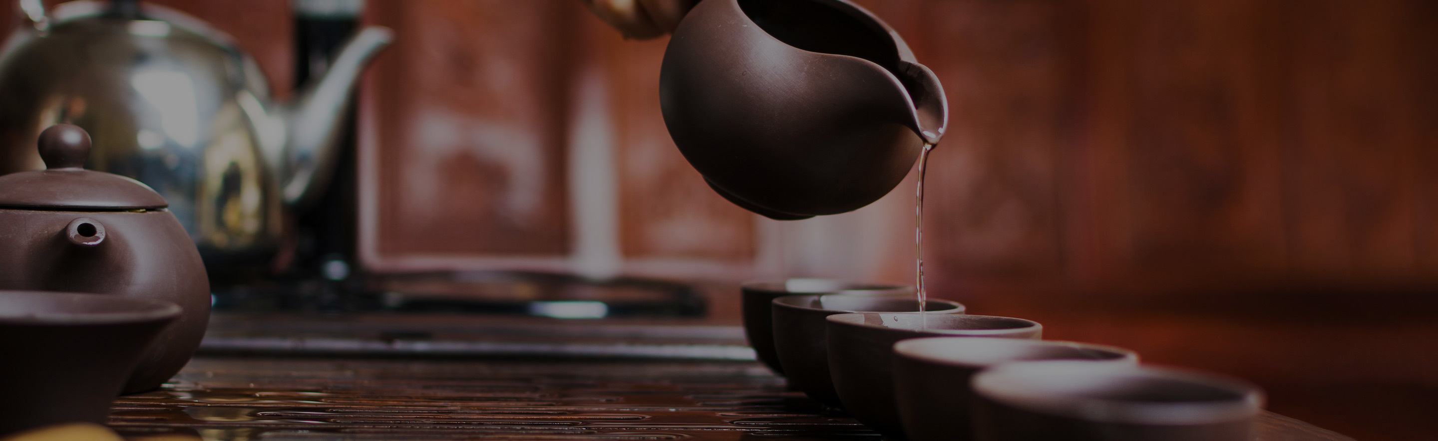 Pouring tea into a series of small cups from a small teapot