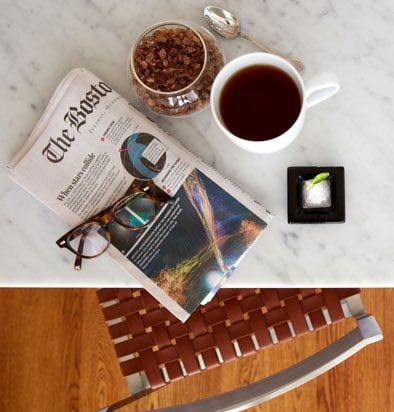 Newspaper and a cup of tea with sugar and a spoon