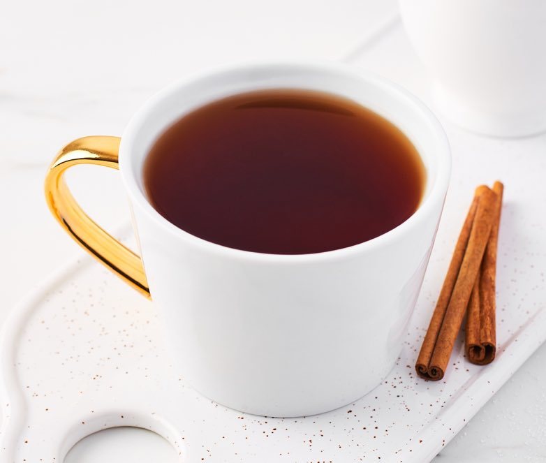 White cup of darjeeling tea with gold handle and cinnamon sticks