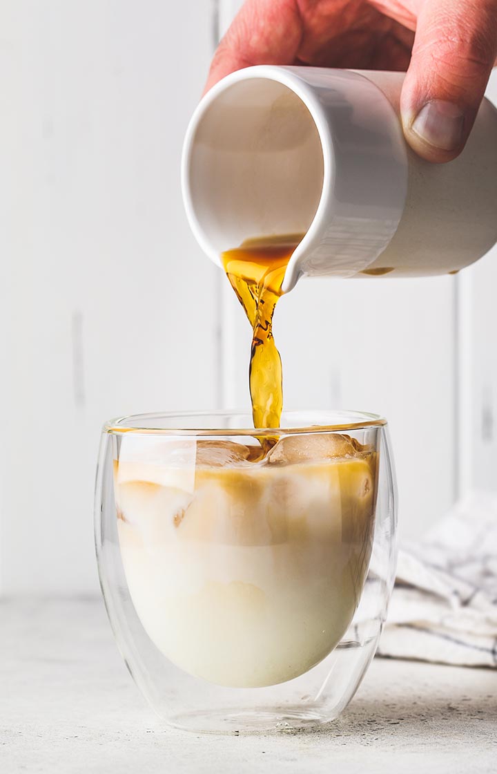 Pouring milk into a iced pumpkin spice latte in a double-walled glass