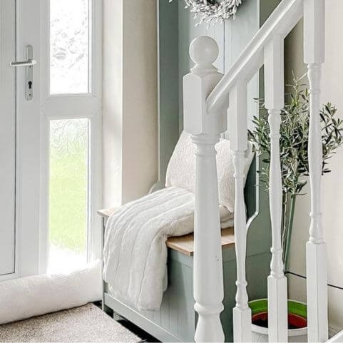 A home entryway decorated with a white staircase, a green storage unit, a potted plant, a white faux fur throw and a white fleece draught excluder.