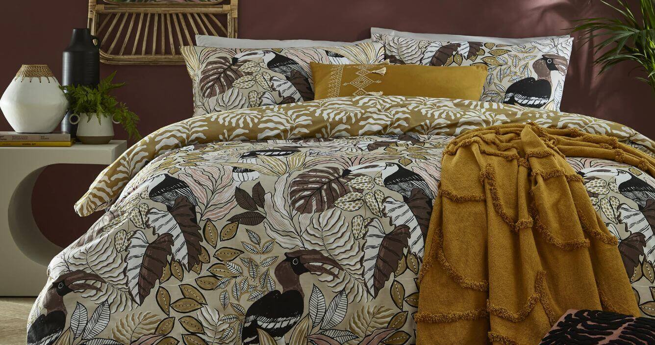 A botanical print bedding set with a yellow tufted throw styled on top. 