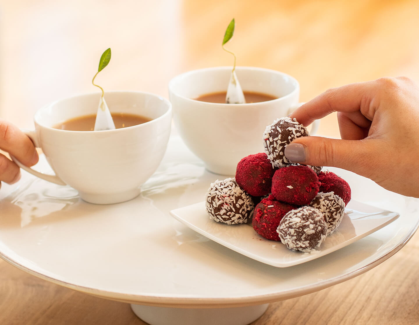 Picking a Raspberry Ganache Truffle off a plate with two cups of tea behind it