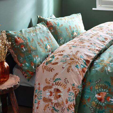A side view of a fern green duvet cover set with an autumnal printed design of leaves, fungi and moths, complete with a coordinating neutral reverse design.