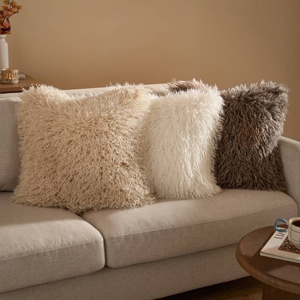 Three faux fur cushions on a beige sofa, in natural, ecru and mocha