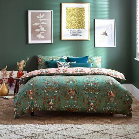 A fern green duvet cover set with an autumnal printed design of leaves, fungi and moths, made on a bed with complementary scatter cushions in a green bedroom.