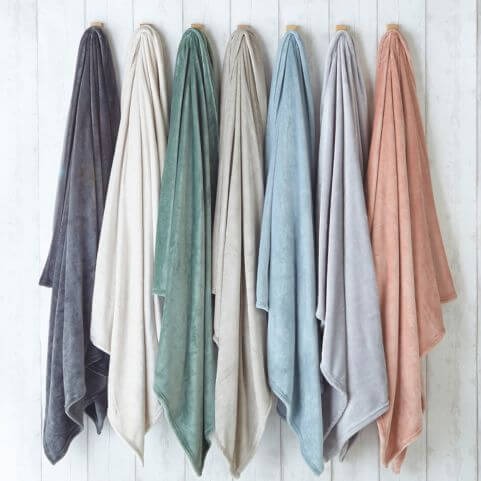 A selection of seven fleece throws in various neutral and muted shades, hung on hooks in a white room.
