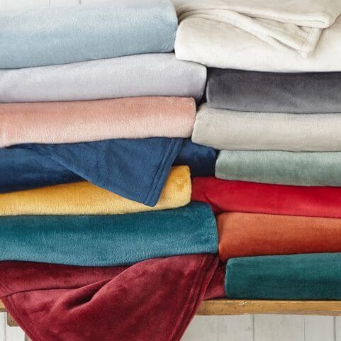 A selection of multiple fleece throws in a range of neutral, muted and bright colours, folded and presented on a wooden surface.