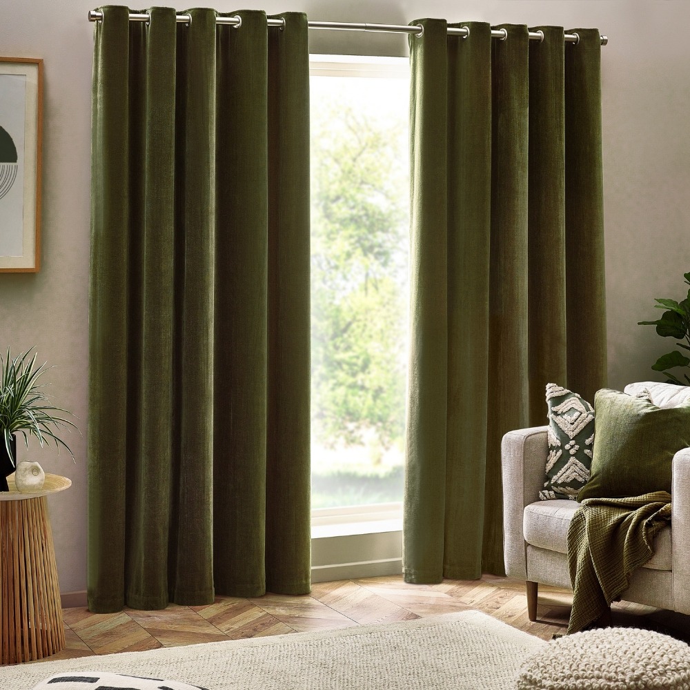 A pair of olive green chenille drapes next to an arm chair with two green cushions and a green cotton throw