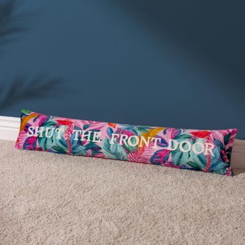 A brightly coloured draught excluder with a multicoloured exotic lead design, laid on a grey carpet in front of a dark blue wall.
