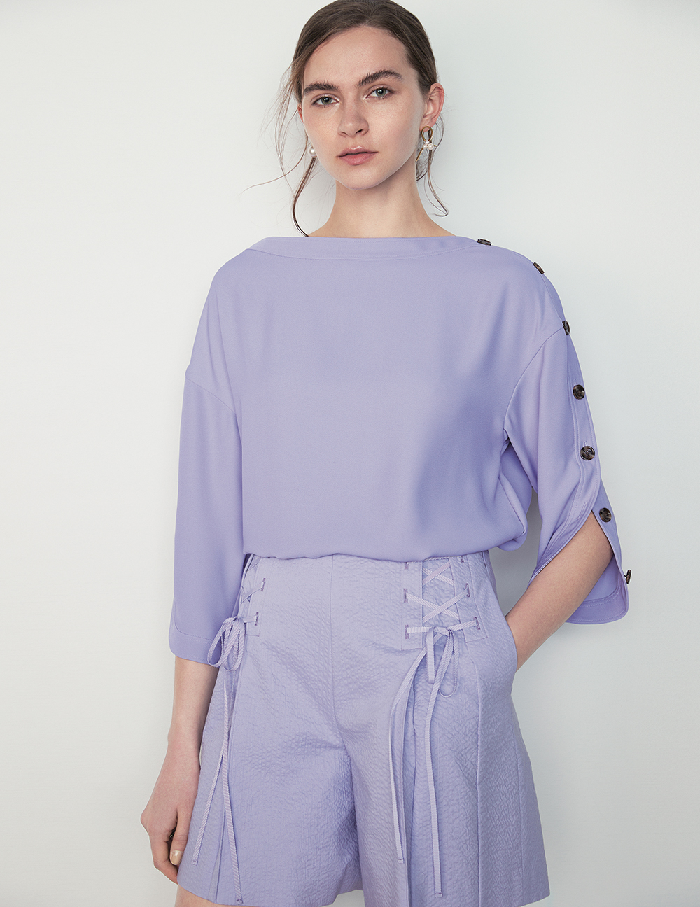 Model in lilac top with buttons down the sleeves and lilac shorts with lace details by the hips 