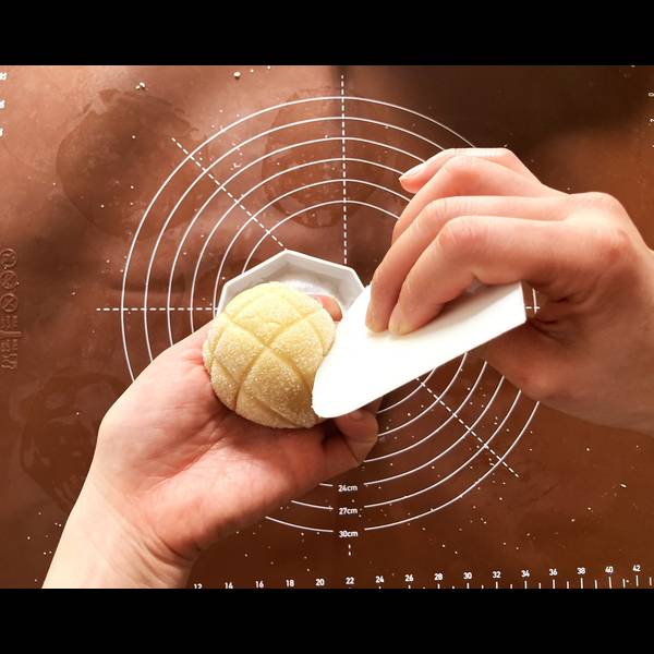 Using a dough scraper to carve lines into the melon pan to give it a melon shape