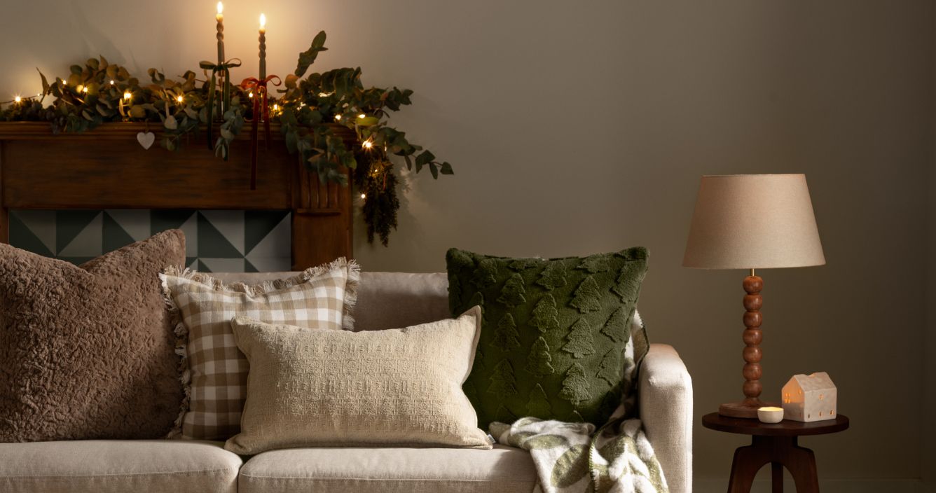 A festive sofa with Christmas cushions, a garland and candle sticks scattered along the back on the mantle piece
