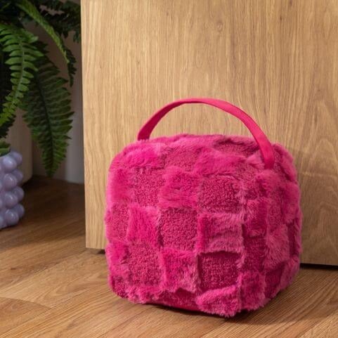 A fuzzy dice style door stop in a hot pink shade, complete with alternating checks of bouclé and faux fur fabric.