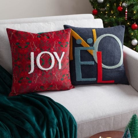 Two modern Christmas cushions in red and navy blue with tufted slogan designs that read 'Joy' and 'Noel'.