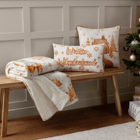 A matching Christmas throw blanket and cushions in clean white shades with printed designs in a luxurious gold shade.