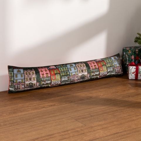 A green Christmas draught excluder cushion with a printed design of a festive town.