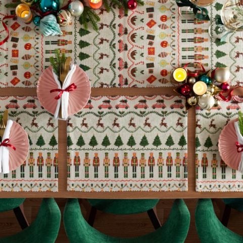 A set of Christmas place mats and a matching table runner with multicoloured designs of reindeer, nutcrackers and more classic seasonal symbols.