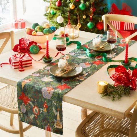 A green Christmas table runner with a traditional printed design of iconic festive decorations.