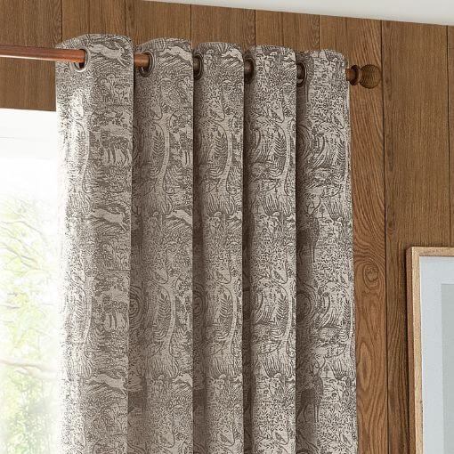 Chenille eyelet curtains with a jacquard winter woods design in a taupe colourway, hung on a wooden curtain pole in a country style room with wood panelled walls.