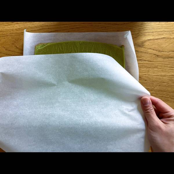 Using another sheet of parchment paper to roll the cake