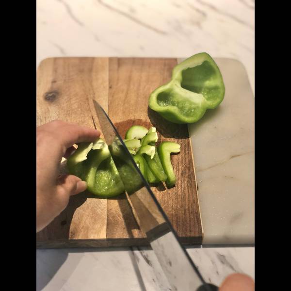 Cutting the green bell pepper in half and then slicing it thinly