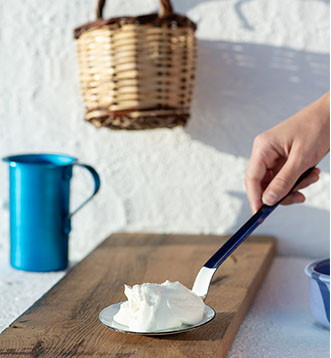 Griechische Küchenszene mit frischem griechischen Joghurt auf einer Küchenkelle gehalten von einer weiblichen Hand