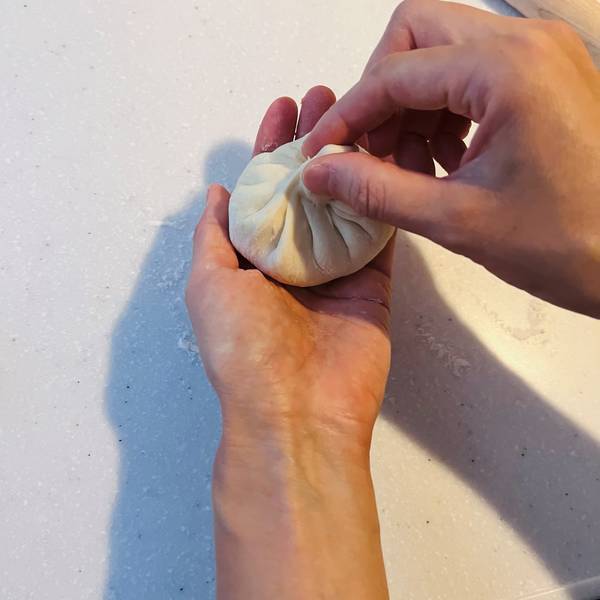 folding the dough towards the center at the top of the nikuman