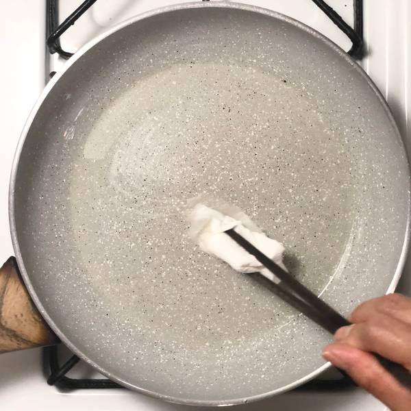 Using chopsticks and a paper towel to evenly grease a fry pan