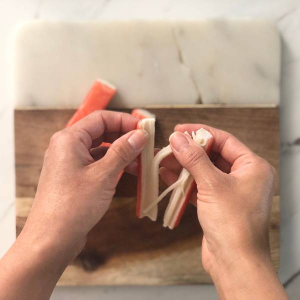 Using fingers to tear immitation crab stick into thin strips
