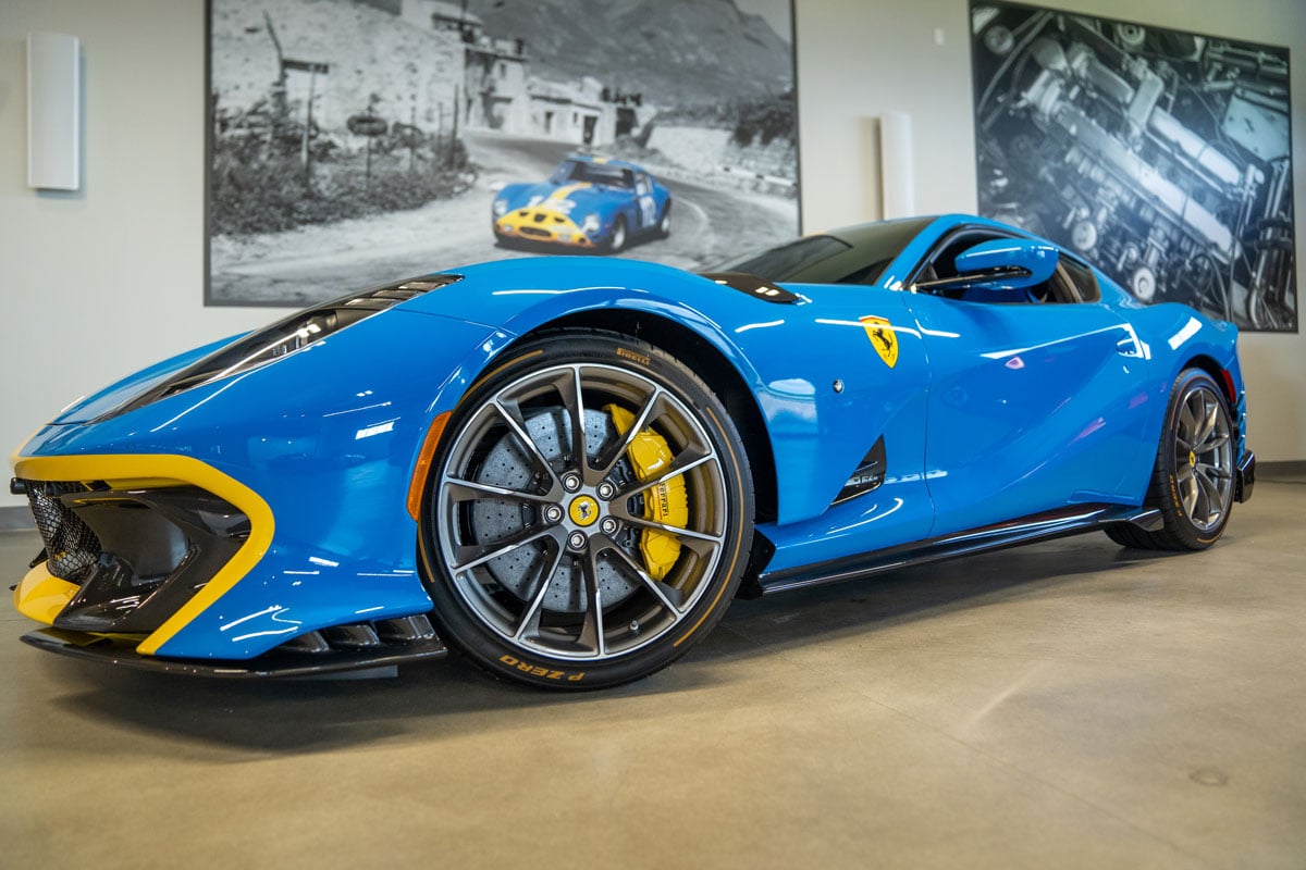 Blue Ferrari parked in front of a large photo of the same car on the wall in a car garage