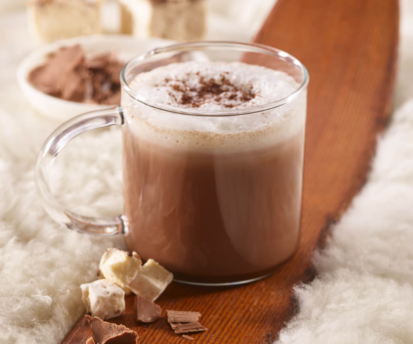 Chocolate Fondue Hot Cocoa in a glass mug on a wooden ski with mini marshmallows and topped with a dash of cocoa powder