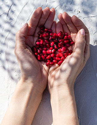Hände auf weißem Untergrund mit roten Granatapfelkernen
