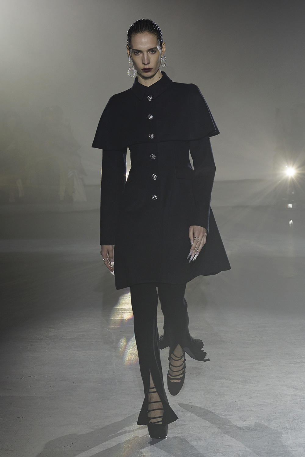 Model wears a black dress with shoulder cuff and black front slit pants