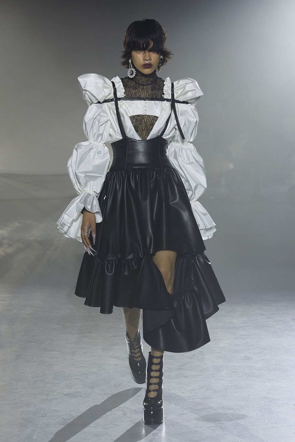Model wears a black lace top under a white puffy long sleeve top and a leather high wasted black skirt. 