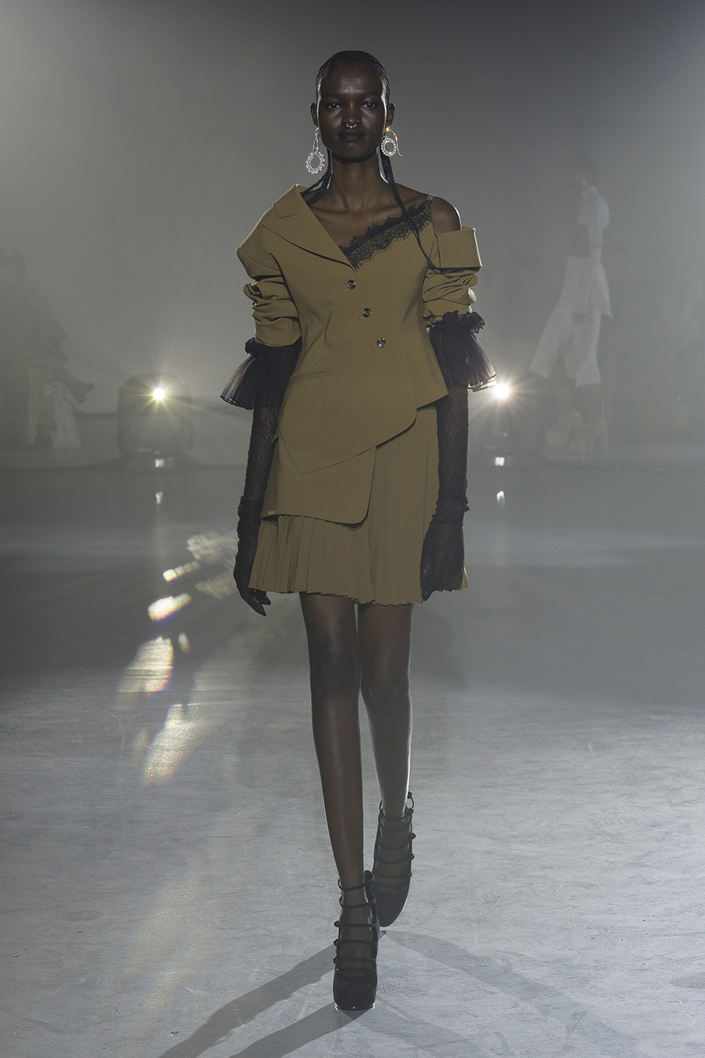 Model wears a dark sand asymmetrical jacket with matching skirt