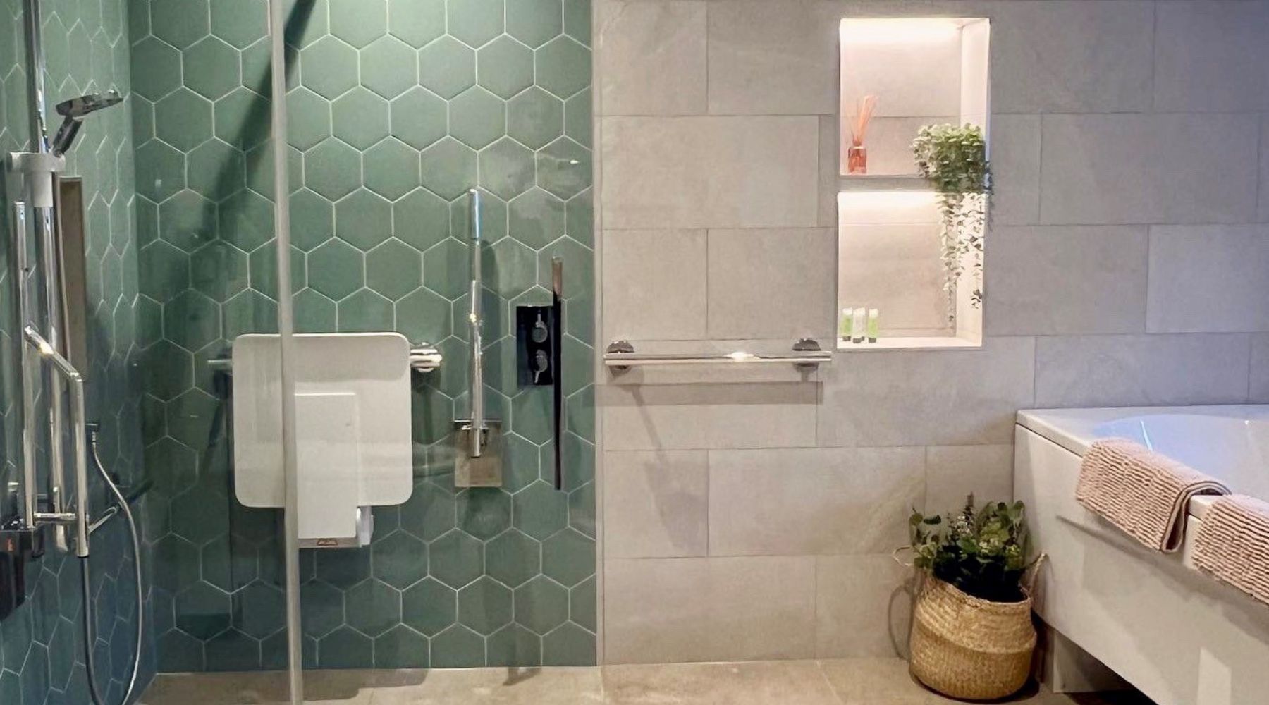 AbleStay's accessible bathroom including hexagon tiles in Timeless Jade, shower arm, hose and valve, bi-folding shower screen, chrome grab rails and wall mounted shower seat.
