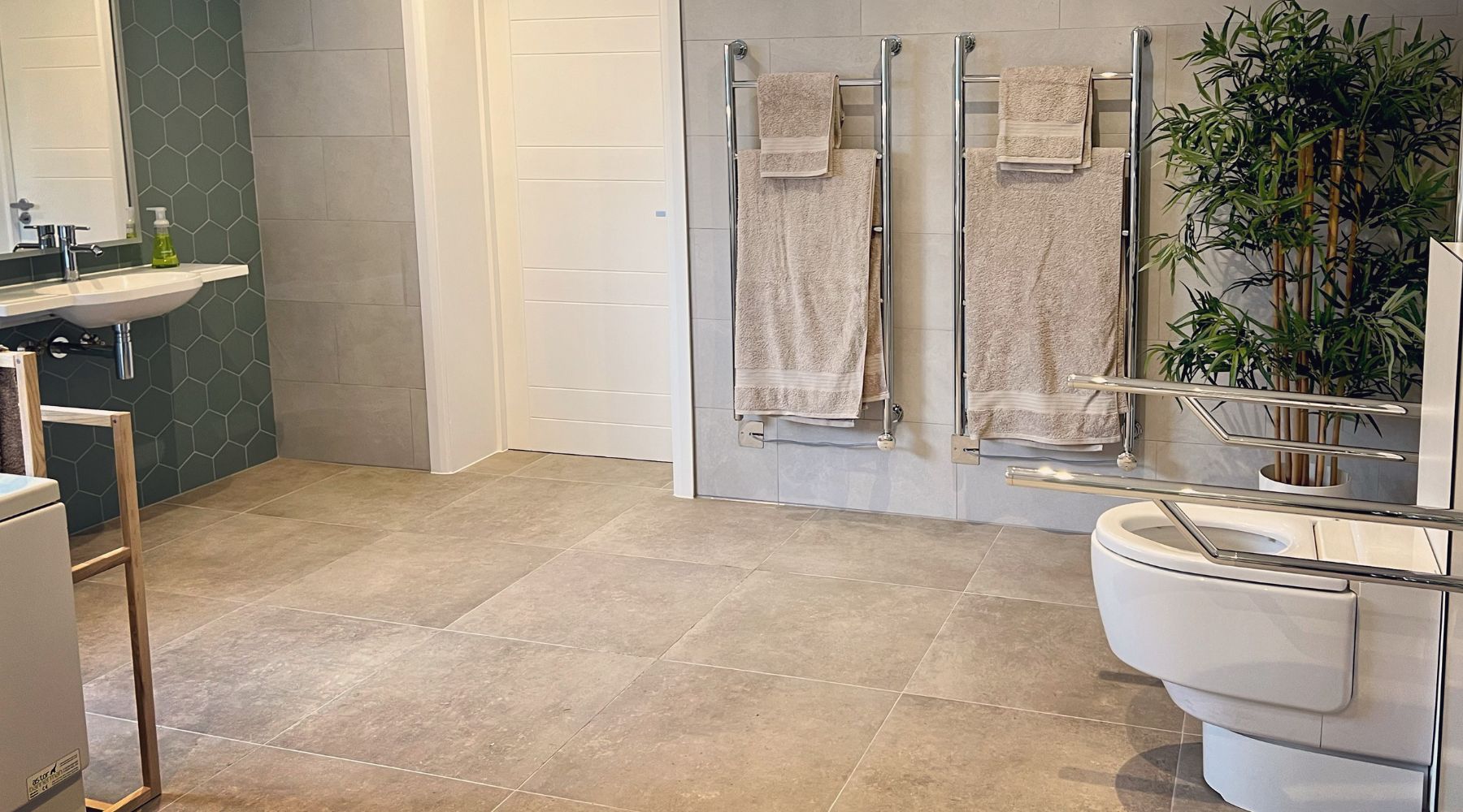 AbleStay's accessible bathroom including toilet, chrome grab rails, wall mounted basin and heated towel rails