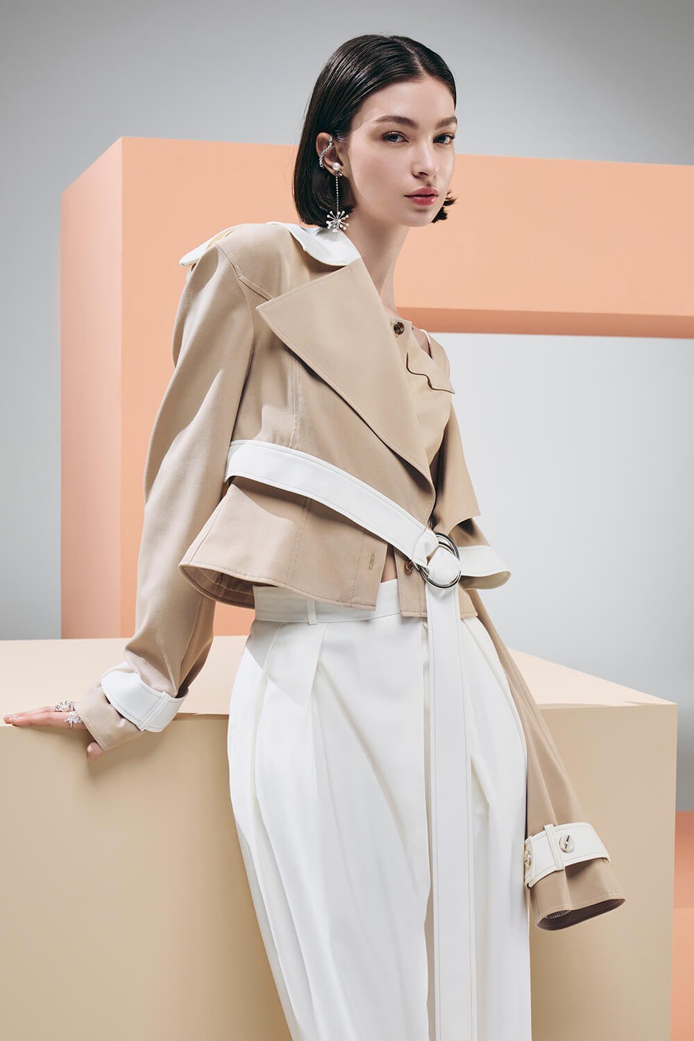 Model wears a cream cropped jacket with white belt details and white trousers
