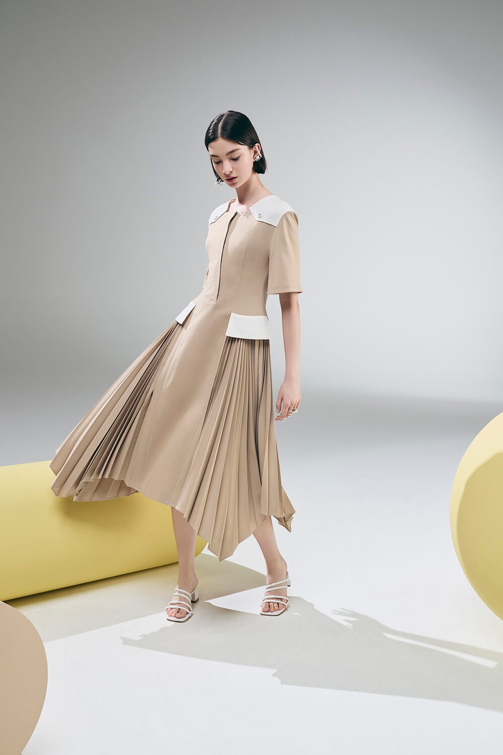 Model wears a long beige dress with white detailing
