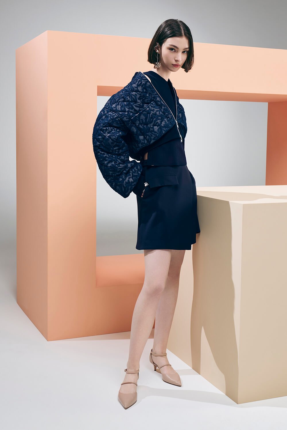 Model wears a navy outfit with a cropped navy jacket, navy skirt and navy tank top