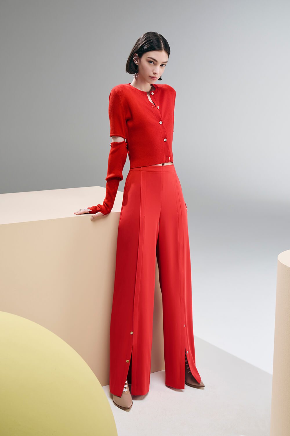 Model wears red pants with slit button details and a button down cropped cardigan