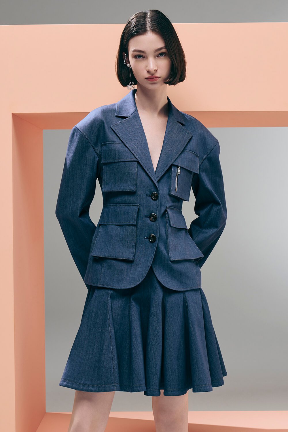 Model wears a navy pleated skirt with a pocket detailed blazer