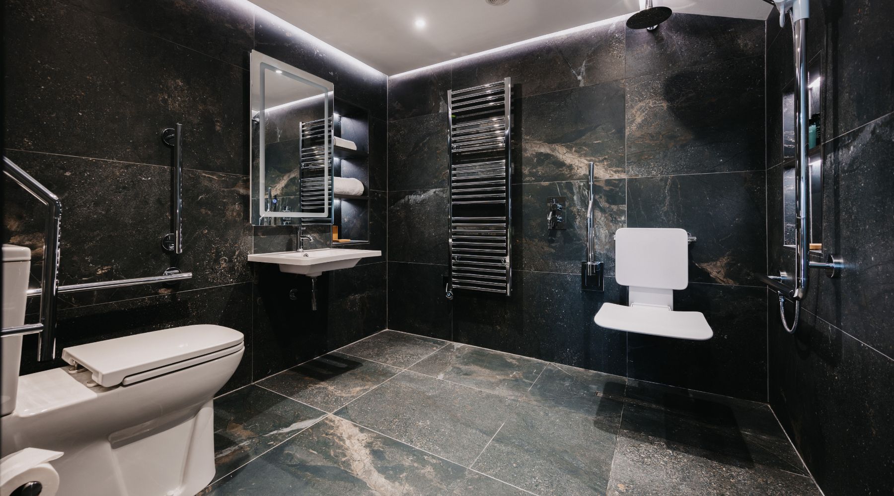 Luxury accessible bathroom with grab rails, wall mounted shower seat and basin, and black and white marble effect tiles