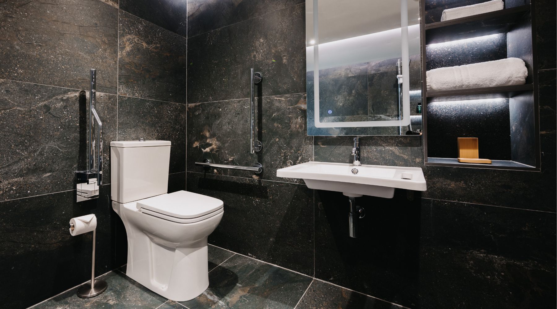 Luxury accessible bathroom with grab rails, wall mounted basin, and black and white marble effect tiles