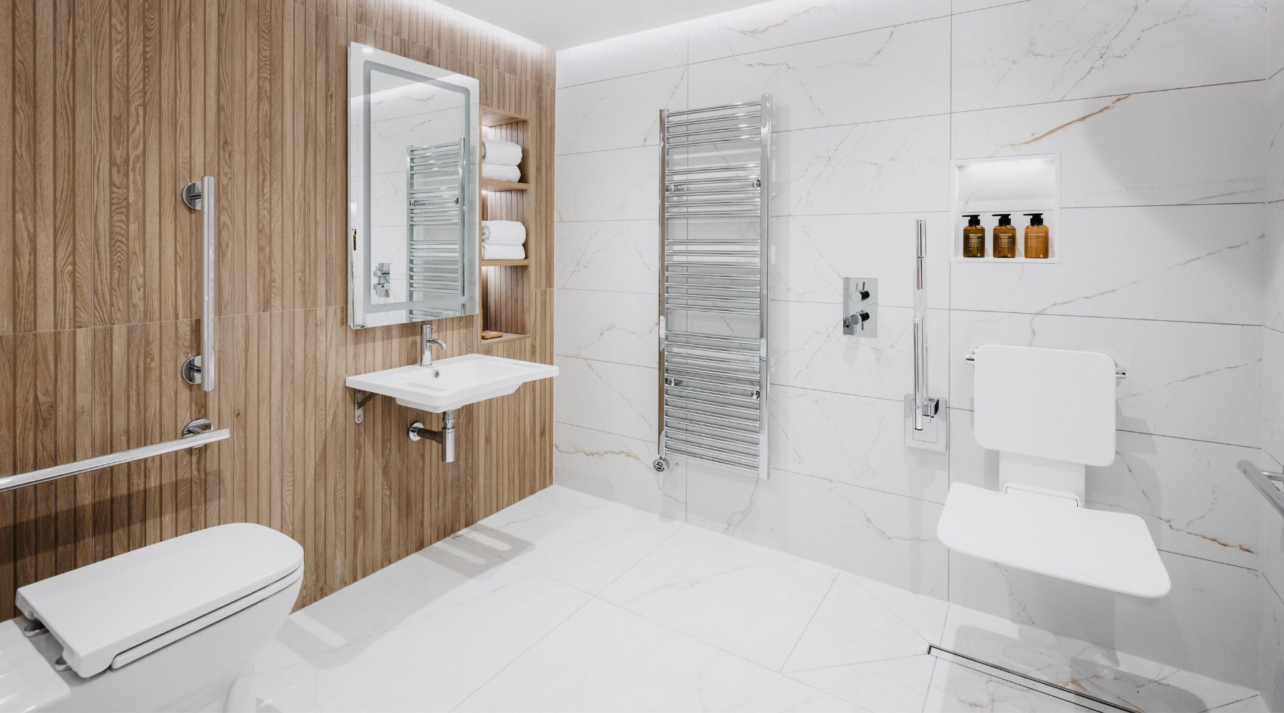 Luxury accessible bathroom with grab rails, wall mounted shower seat and basin, white marble tiles and natural wood panelling 