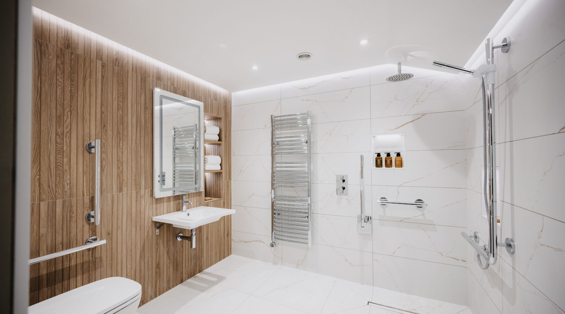 Luxury accessible bathroom with grab rails, wall mounted basin, white marble tiles and natural wood panelling 