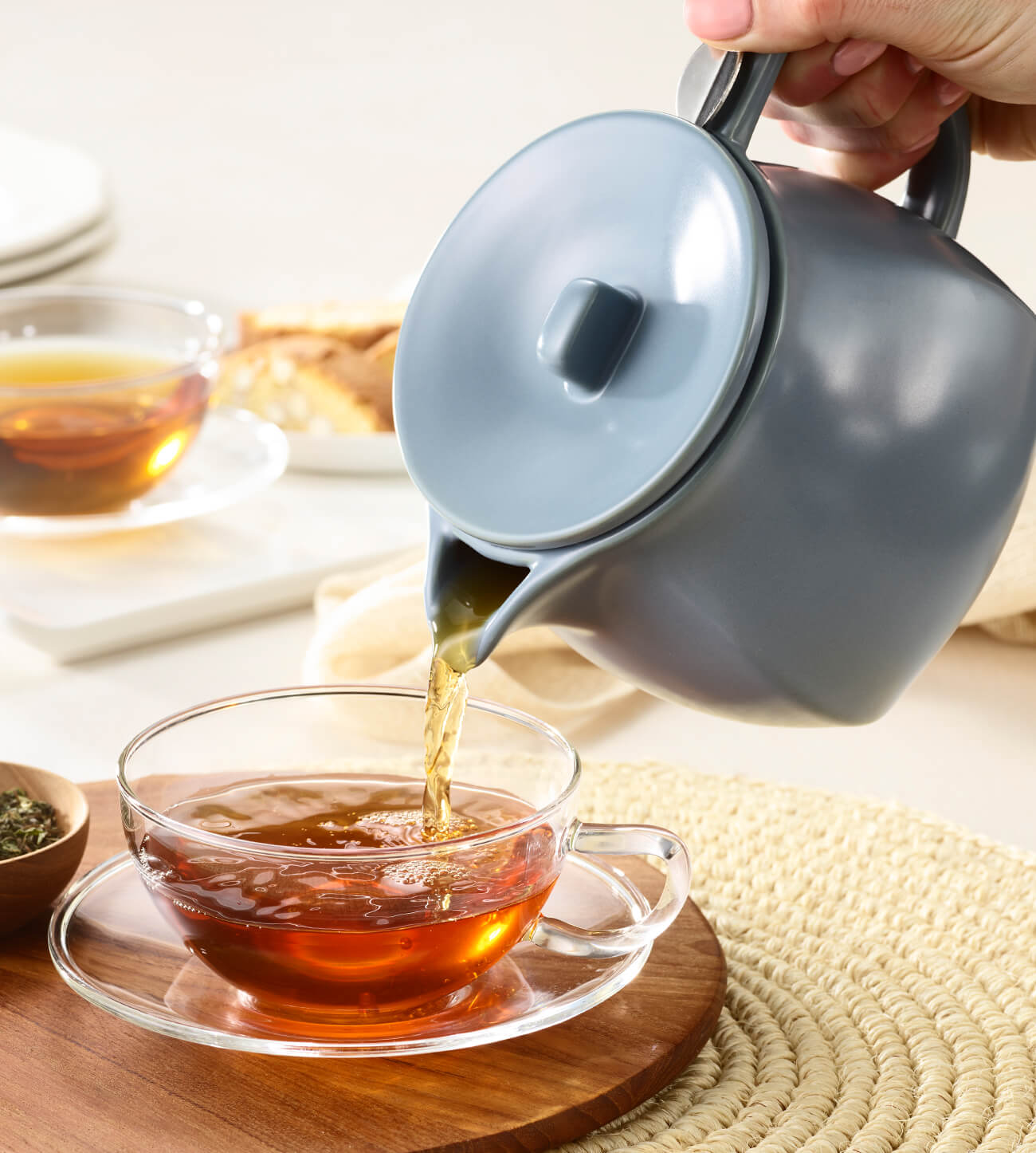 Pouring tea from teh Fiore Teapot into a glass cup on a wooden tray