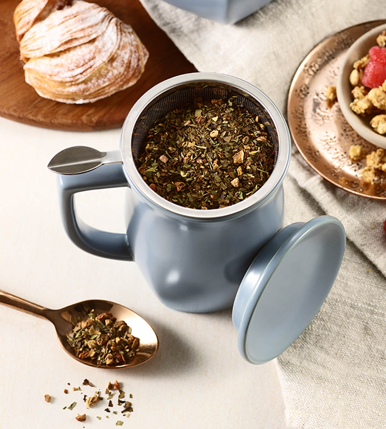 Fiore Steeping cup with loose tea in the basket, see from above with a spoon of loose tea and a croissant