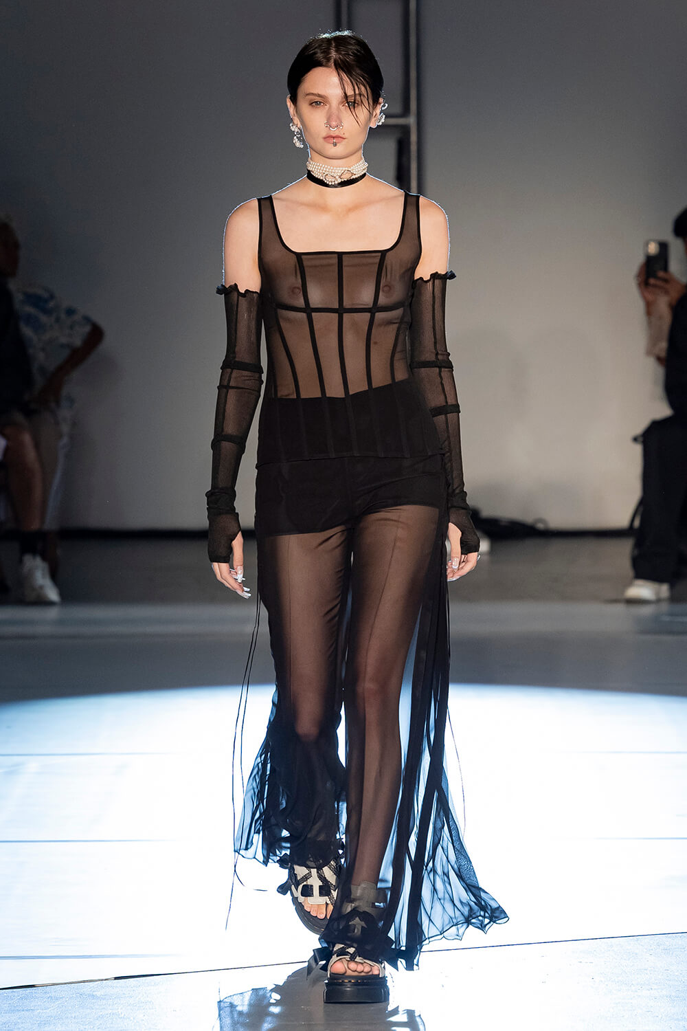 Model wears a black see through corset top with see through black pants and arm warmers
